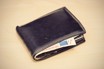 leather wallet with 50 Euro banknote inside on wooden table, vintage filtered style