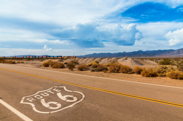 U.S. Route 66 highway, with sign on asphalt and a long train in the background, near amboy, california. Located in the mojave dessert
