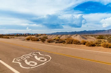 Poster US Route 66 Highway, met bord op asfalt en een lange trein op de achtergrond, in de buurt van Amboy, Californië. Gelegen in het mojave-dessert? © Michael Urmann