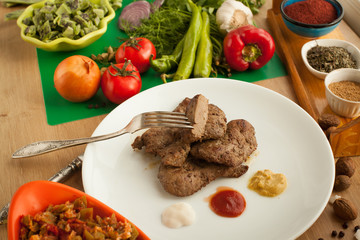 Roast meat served with ketchup, mayonnaise and mustard, sliced piece of meat hanging on a fork. Cooked liver with spices on white plate. Vegetables vs meat.