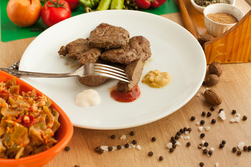 Roast meat served with ketchup, mayonnaise and mustard, sliced piece of meat hanging on a fork. Cooked liver with spices on white plate. Vegetables vs meat.