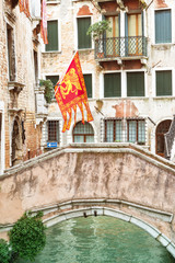 Tranquil canal with a bridge and venetian flag in Venice (Italy). Vertically.