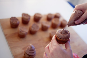 The girl covers the cake with cream. Process of cooking cupcakes, muffins and ingredients for decoration on the table. woman's hand holds one cupcake
