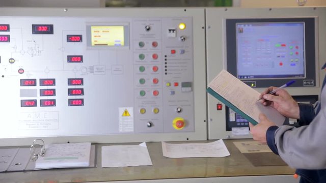 Engineer controls parameters on a control panel at a industrial factory. Writing indications, measure into pad. HD.
