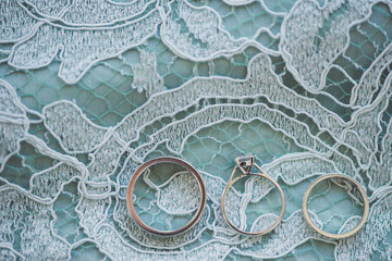 wedding rings and engagement ring on turquoise lace background