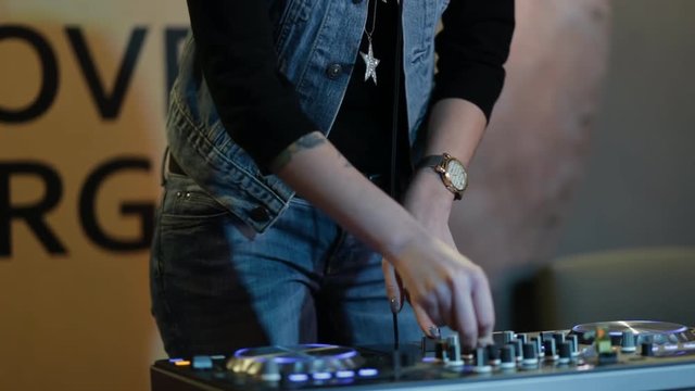 Woman DJ tweak different track controls on dj's deck at nightclub, cropped shot