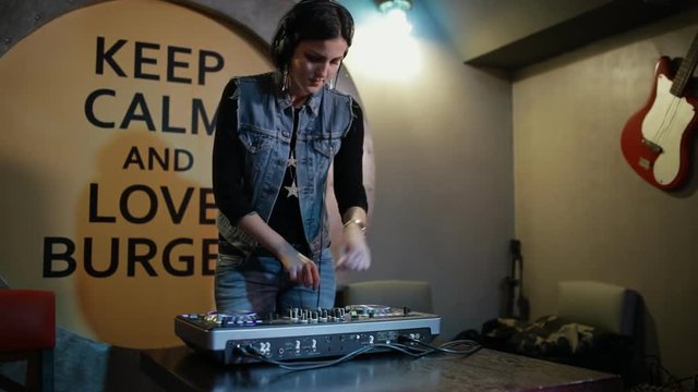 Woman DJ tweak different track controls on dj's deck at bar