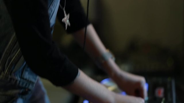 Female hands of DJ tweak track controls on dj's deck, camera is breathing