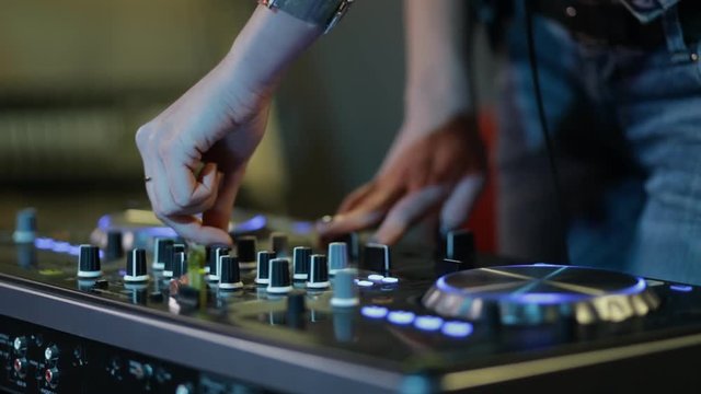 Female hands of DJ tweak track controls on dj's deck, camera is breathing