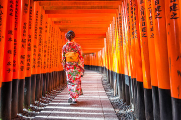 Women in kimono stand at Red Torii gates in Fushimi Inari shrine, one of famous landmarks in Kyoto,...