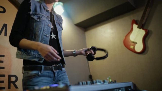 Woman DJ tweak different track controls on dj's deck at nightclub
