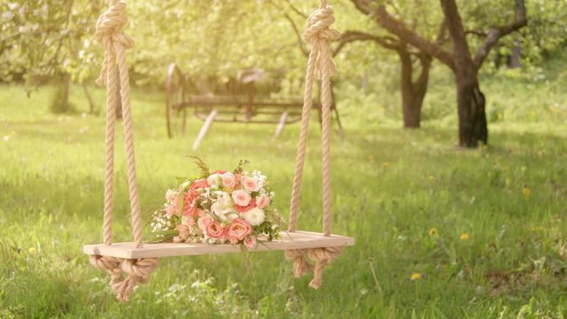 Flowers on wooden swing under blossoming apple trees, sun flare