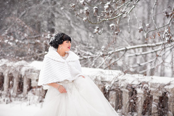 Obraz na płótnie Canvas Winter wedding portrait. Portrait of beautiful bride, who is wearing a white coat against the background of the fairy forest in snowy weather