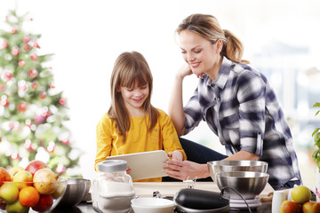 Christmas time. Portrait of cute daughter and her mom baking christmas cookies together in the kitchen.