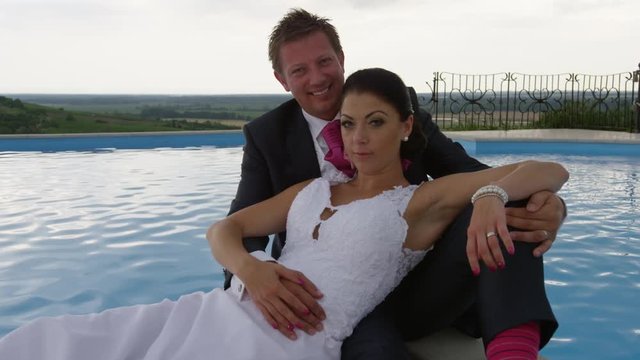 A newly married couple look into the camera as they pose for photos by an infinity pool at a vineyard in the Czech Republic. 4k. In slow motion.