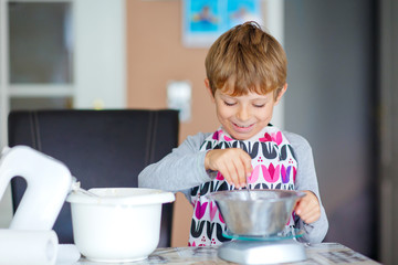 Funny blond kid boy baking cake indoors
