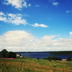 Fototapeta na wymiar Small village near Kenozero lake. View from the hill. Summertime meadows. Suny summer day. Journey to the north of Russia. Kenozersky National Park (UNESCO Biosphere Reserve).