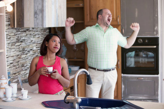 Woman In Kitchen Looking Annoyed While Man Is Yawning