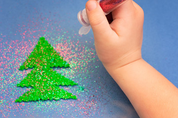 children's hands sprinkled with glitter Christmas tree cut out of plush on blue paper background