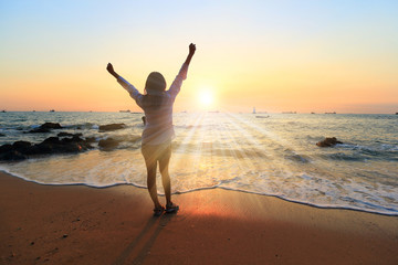 Fototapeta na wymiar Freedom winning woman cheering at sunset beach. Success concept with female adult from the back arms up at the sky looking at the ocean feeling free and successful. Achievement of her life.