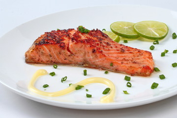 Close up of grilled salmon topped minced shallot ,mayonnaise and sliced lemon on white dish. Selective focus