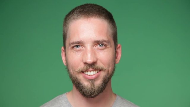 Close up young hipster man with mustache and beard smiling against chroma key green screen background