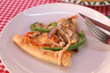 Slice of vegetarian pizza with cheese, tomato sauce, green peppers, mushrooms and onion in a pizzeria. Selective focus. 