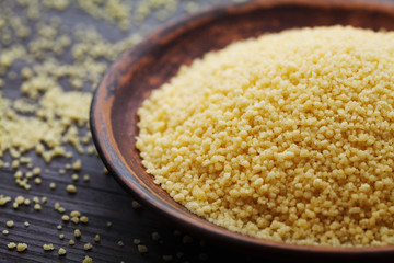 Raw couscous in bowl on dark wooden table