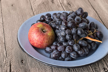 Naklejka na ściany i meble Apple and grapes. Apple and bunch of grapes on a metal dish on a gray wooden table.