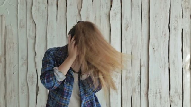 Woman listening to music, dancing and shaking her long hair. White wooden background