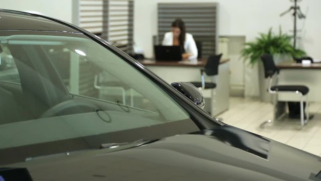 Work in the showroom. Sales Manager at the dealership works at a Desk. In the foreground of the car, the image Manager is blurred.