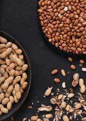 Shelling in process with a pile of shelled and unshelle draw peanuts on black rustic background. Healthy food. Top view.