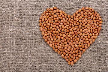 Organic peanuts in heart symbol on rustic jute fabric with copy space. Canvas background. Top view.