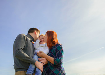 Family of three huging and kissing on the sky background.