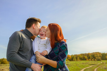 Obraz premium Family of three huging and kissing on the sky background.