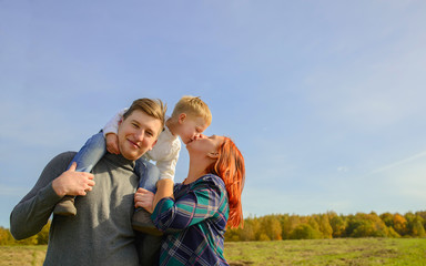 Family of three huging and kissing on the sky background.