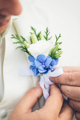 groom's hand arranging boutonniere flower on suit