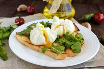 Boiled eggs in a pouch (poached) on crispy toast and green arugula leaves. Dietary breakfast.