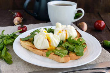 Boiled eggs in a pouch (poached) on toast and crisp green leaves of arugula and a cup of tea. Dietary breakfast.