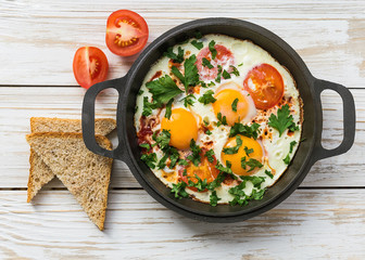 Pan of fried eggs, tomatoes and parsley with bread