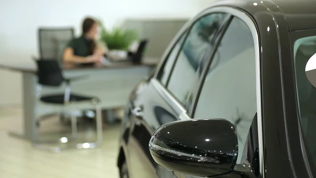 Work in the showroom. Sales Manager at the dealership works at a Desk. In the foreground of the car, the image Manager is blurred.