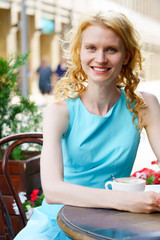 Smiling young blond woman in cafe with cup of cappuccino