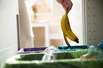 Woman putting banana peel in recycling bio bin in the kitchen. Person in the house kitchen...