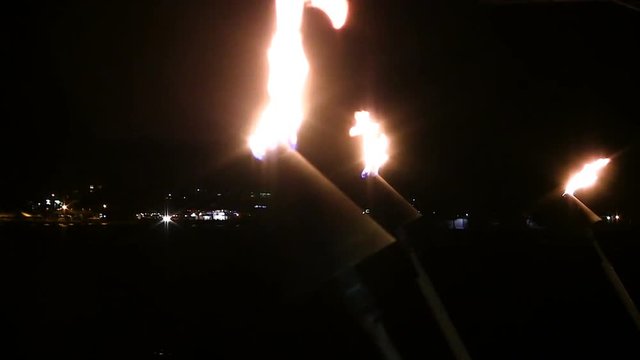 Gas Flame Torches Burning In Night Sky With Building Lights In Background

