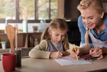 Smiling beautiful woman drawing with her daughter in the kitchen