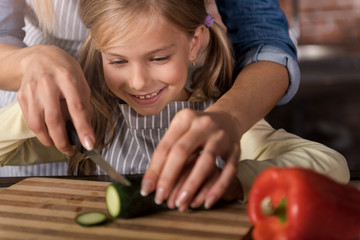 Smiling involved girl cutting a cucumber with her mother