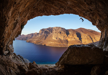 Male rock climber hanging with one hand while climbing in cave