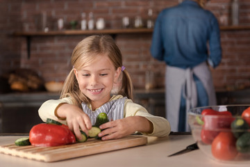 Fototapeta na wymiar Smiling little girl touching vegetables in the kitchen