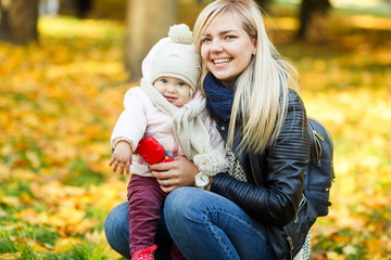 Happy young mother with daughter in park among yellow trees
