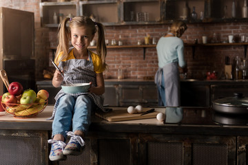 Delighted girl mixing eggs on the table in the kitchen